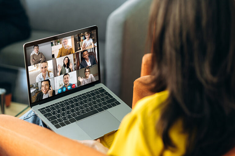 Laptop monitor view over female shoulder during group video call with multi-ethnic international business colleagues discussing about future financial plans and strategy